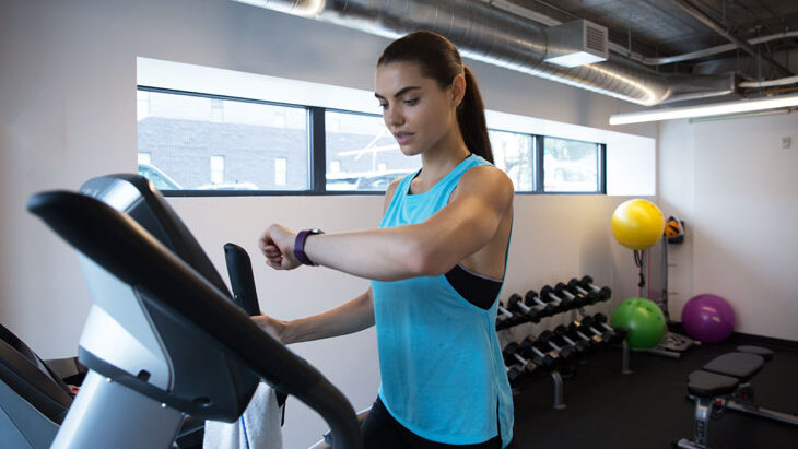 A woman using her fitbit while performing a treadmill activity.